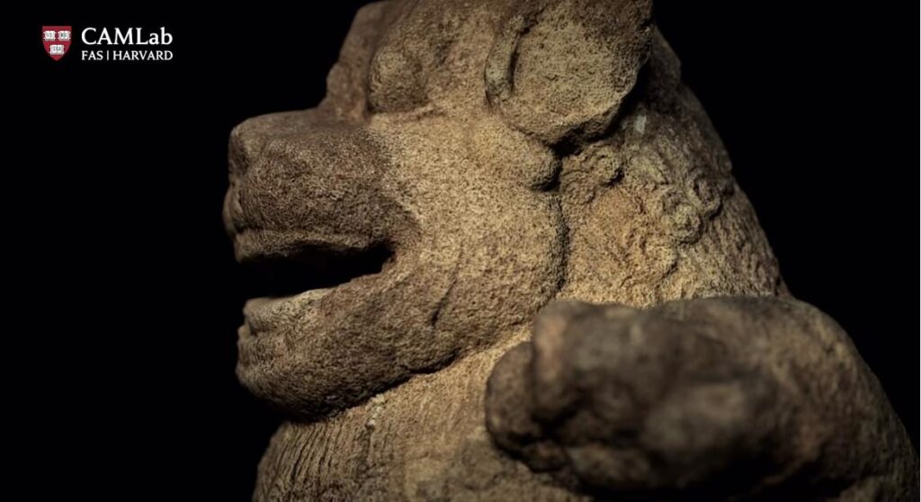 Close up of a weathered stone head sculpture against a black background camlab harvard logo in the top left corner